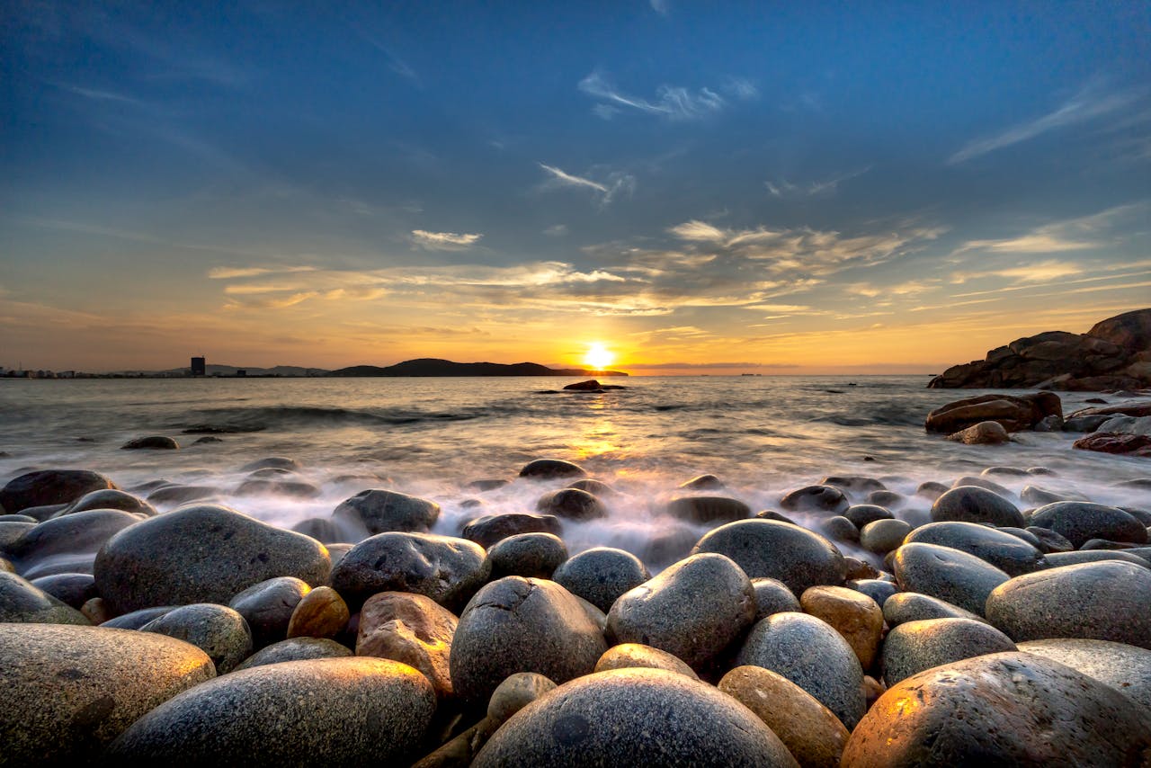 Home Serene rocky shore landscape featuring a stunning sunset over the ocean with dramatic clouds.